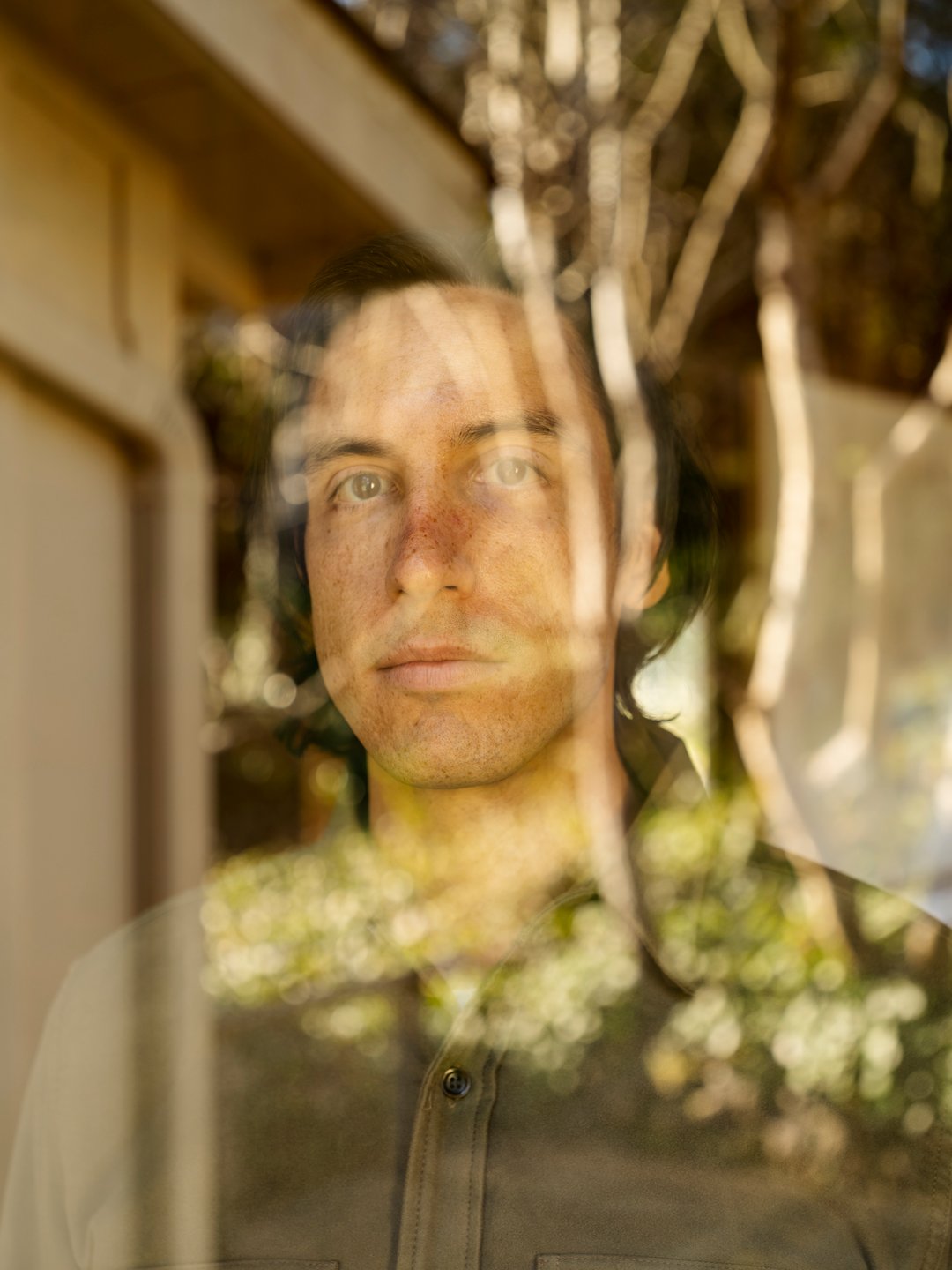 This photograph of Josh was taken from the other side of a window. We can see trees and leaves reflected in the window, which lends a kind of blurring effect to his face.