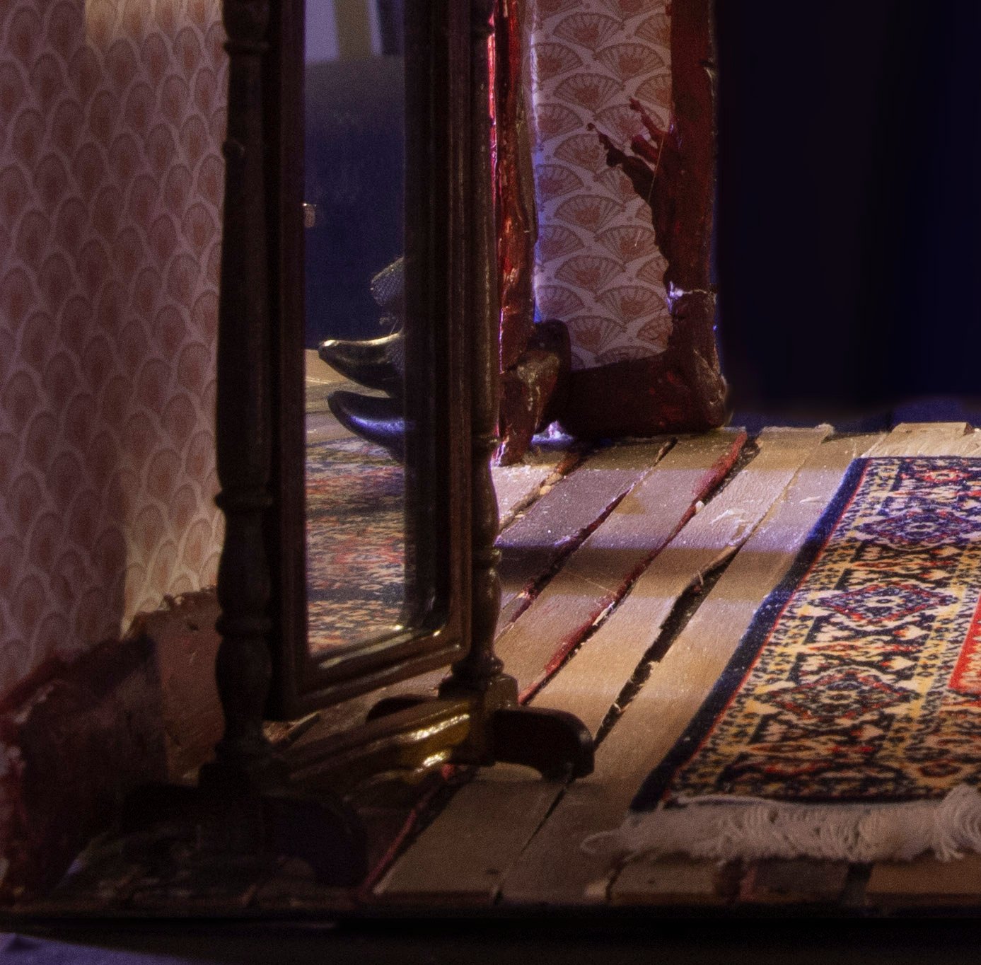 This photograph is a close up of the floorboards and rug the in the diorama. A tiny mirror shows us a peek of Lizzie's father's shoes hanging off the couch.