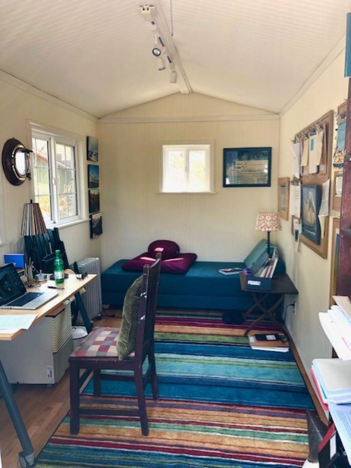 This photograph shows the inside of the writer's garden shed, which she explains in the piece. We see a desk and a day bed and pictures hung up on the wall.